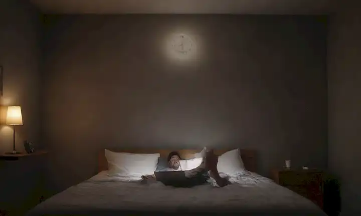 Teléfono 3D flotando a mitad del aire, con un fondo oscuro de la habitación, reloj brillante cerca, una persona relajante en una cama con un ordenador portátil abierto pero inactivo, suave iluminación y sombras para transmitir somnolencia
