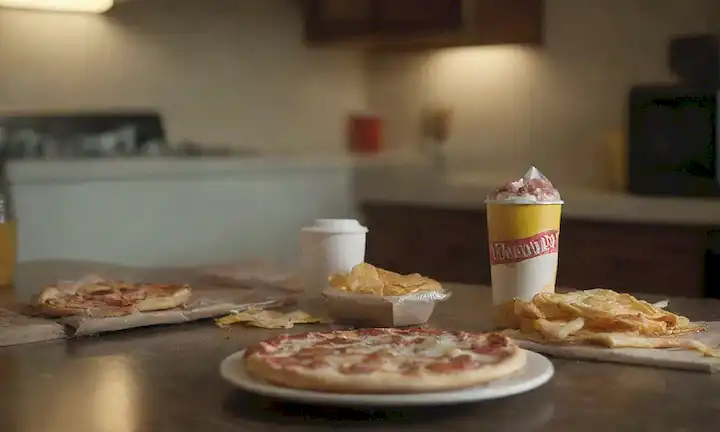 opciones de comidas poco saludables, aperitivos azucarados, alimentos procesados, envolturas de comida rápida, bebidas de calorías vacías, una persona con mala postura, una cocina desordenada y desordenada, una bolsa de patatas fritas, una caja de pizza, una botella de soda