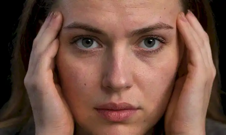 Un retrato de cerca de una persona cara con cejas surcadas, ojos cansados y labios purgados en concentración; un débil resplandor en la frente como si a partir de un intenso esfuerzo mental, contra un fondo oscuro o mudo con sutiles sombras de gradiente; las manos apretadas en puños descansando en las rodillas con uñas cavando suavemente en la piel