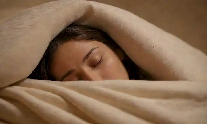 Una escena nocturna serena con una persona dormida acurrucada bajo una manta, rodeada de suave iluminación y colores calmantes, con sombras sutiles en la cara para transmitir la relajación, con una suave línea de drool que forma desde la esquina de su boca, en medio de un fondo minimalista con pocos patrones delicados, que transmiten un sentido de tranquilidad y tranquilidad
