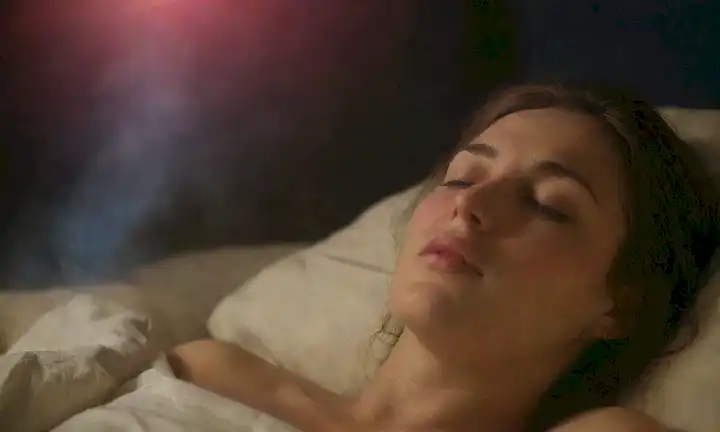 Una escena nocturna serena con una persona durmiendo, suaves corrientes de aire, y sutiles wisps de saliva cayendo de su boca, suspendida en el aire medio alrededor de su cara, un toque de niebla o niebla que los rodea, suave iluminación desde arriba, sin distracciones ni elementos audaces