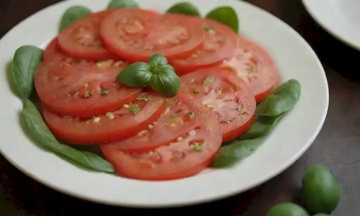 Calabacín y tomates frescos en un plato, rebanados finamente y dispuestos en un patrón armonioso, adornados con hojas de albahaca, deslumbrados con aceite de oliva, fondo ligeramente borroso, paleta de color cálido, presentación apetitosa, composición artística