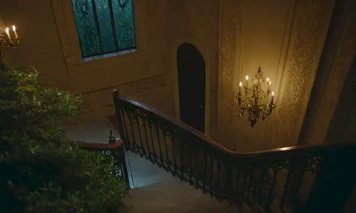 Una mansión grande, ornamentada con una escalera de viento, pasillos diminutos iluminados, y habitaciones con puertas cerradas; una llave está escondida en un arbusto cercano, mientras que una luz tenue de un cuarto lejano; una figura desaparece en las sombras, dejando sólo susurros detrás