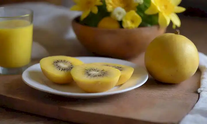 un kiwifrut amarillo vibrante rebanado en la mitad, situado en una mesa de madera rústica con una cálida iluminación de desayuno, rodeado de un delicado ramo de flores frescas, una manta suave o placemat con textura sutil, y un toque de luz natural de la mañana