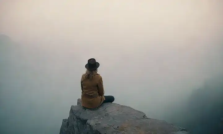 Una persona perdida en el pensamiento, de pie en el borde del acantilado con gran paisaje, rodeada de niebla, sosteniendo un reloj de hora, usando un sombrero, sentado en una roca, mirando a la distancia, con iluminación sutil y colores mudos
