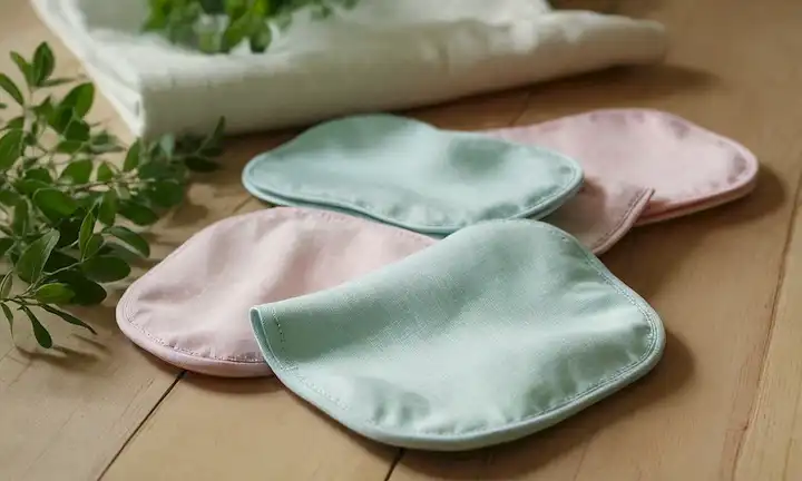 un plano de reutilizables almohadillas de tela sobre una mesa de madera, rodeada de vegetación, con un fondo sutil gradiente, con suaves tonos pasteles, con un toque de luz solar mirando a través, transmitiendo un sentido de naturalidad y serenidad