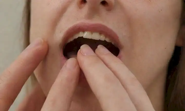 Cierre de la mano con uñas mordidas, cutículas divididas y enrojecimiento; otro ángulo que muestra los dedos entrelazados, la boca abierta y los dientes agarrando el clavo; o una ilustración de una persona sentada sola, la cabeza inclinada, con la mano escondida detrás del pelo, transportando el secreto y la culpa