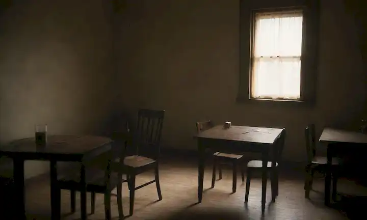 3 personas en una pequeña habitación, sombras y oscuridad prevalecen, sillas vacías y mesas dispersas alrededor, una fuente de luz débil en la esquina, sutiles toques de desorden y caos, sensación general de malestar y malestar, sin rostros sonrientes