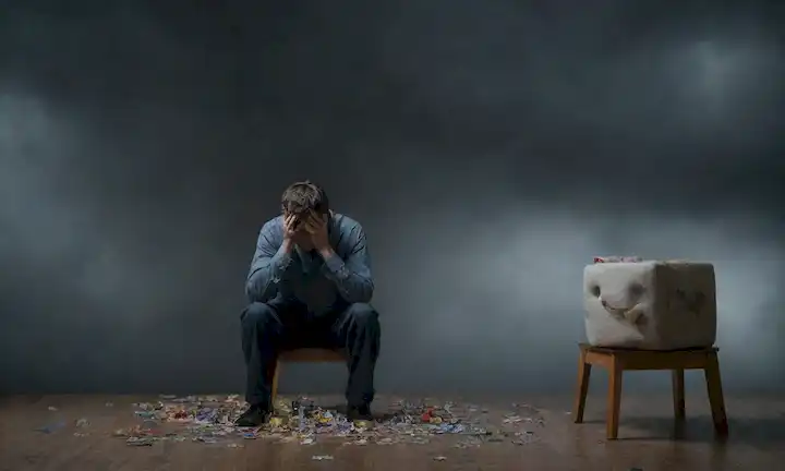 Una persona sentada en una silla con la cabeza en sus manos, rodeada de nubes oscuras, juguetes rotos y puzles, con lágrimas surgiendo en sus ojos, transmitiendo un sentido de desesperación, mientras una luz débil brilla en el fondo para representar la esperanza de soluciones