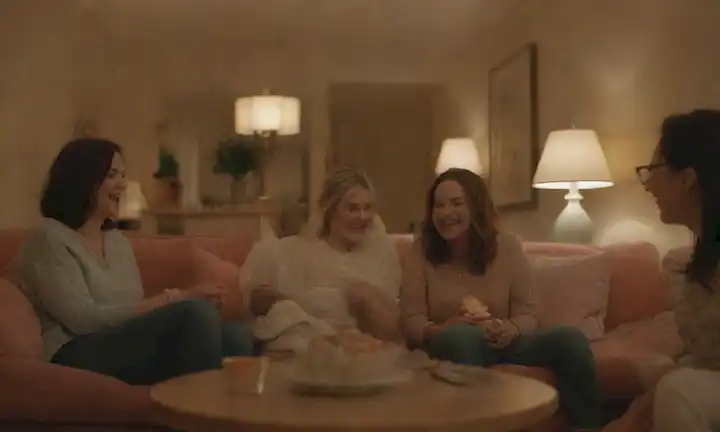 3-5 mujeres, riéndose y charlando en voz alta en un acogedor salón, rodeado de objetos decorativos y muebles cómodos, con iluminación suave y acentos coloridos, transmitiendo un sentido de calidez y camaradería