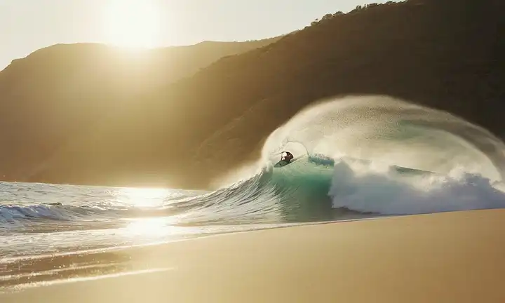 olas que chocan contra la playa de arena, velero que se desliza a través del agua turquesa, viento soplando a través del pelo marinero, luz del sol que refleja ondas, surfistas determinada expresión, brisa del océano que azota a través de hilos de pelo