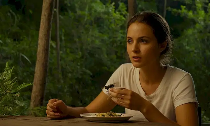 Una persona en atuendo casual, al aire libre, día o noche, sin pulverización de insectos visibles o repelente; un enjambre de mosquitos que se mueven alrededor de ellos, tratando de morder; la persona que come o bebe tranquilamente algo de un plato o un cristal, apareciendo completamente nonchalant sobre los insectos zumbidos; el entorno circundante es natural (por ejemplo, bosque, playa, etc), con algunas plantas y árboles en el fondo; sensación de relajación es una de tranquilidad